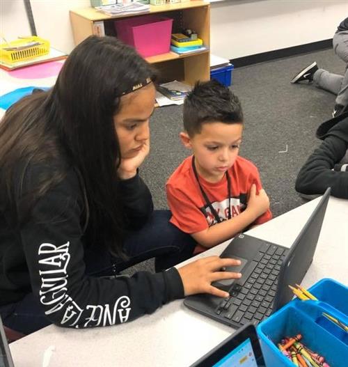 an older student and a young student  work on a computer